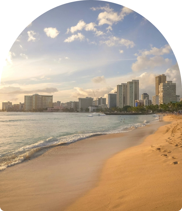 Sunny beach with city skyline and gentle waves at sunset.