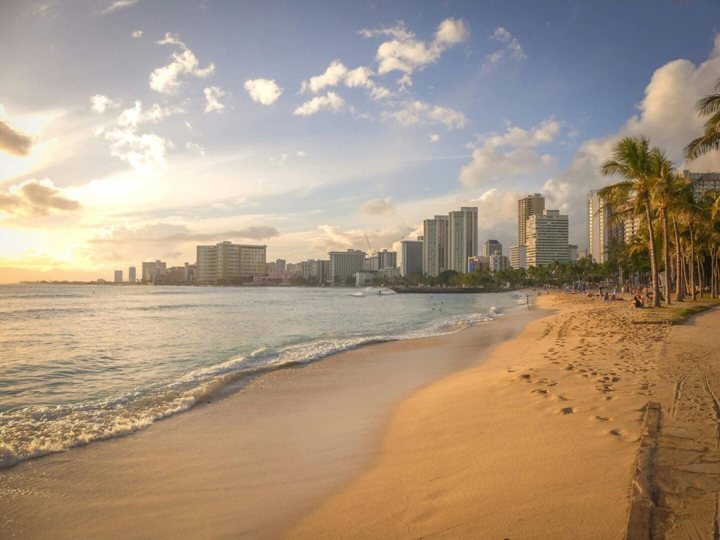Sunset over a sandy beach with city skyline in the background.