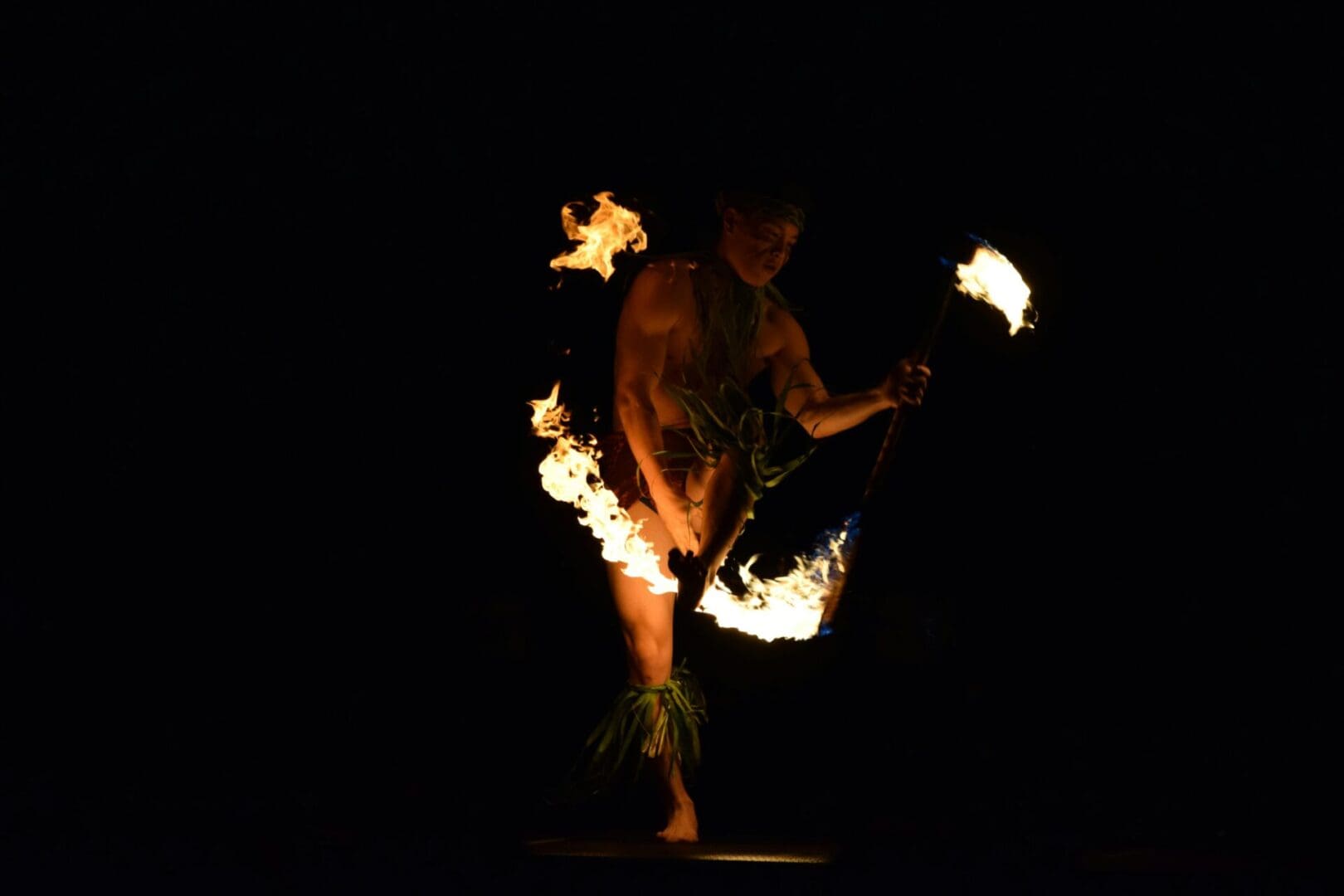 A performer skillfully twirls flaming torches in the dark.