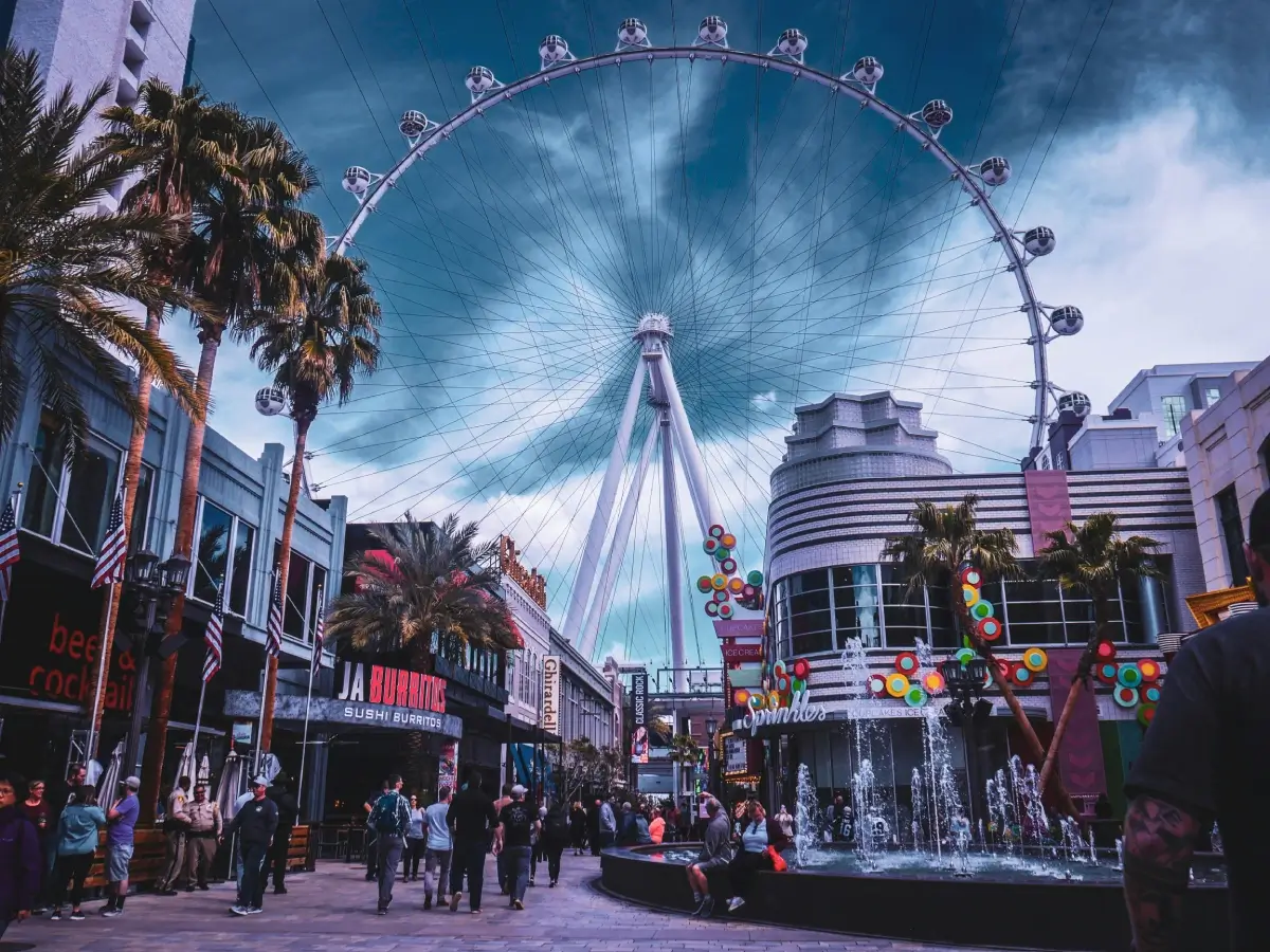A bustling street view with the High Roller Ferris wheel in Las Vegas under a dramatic sky.