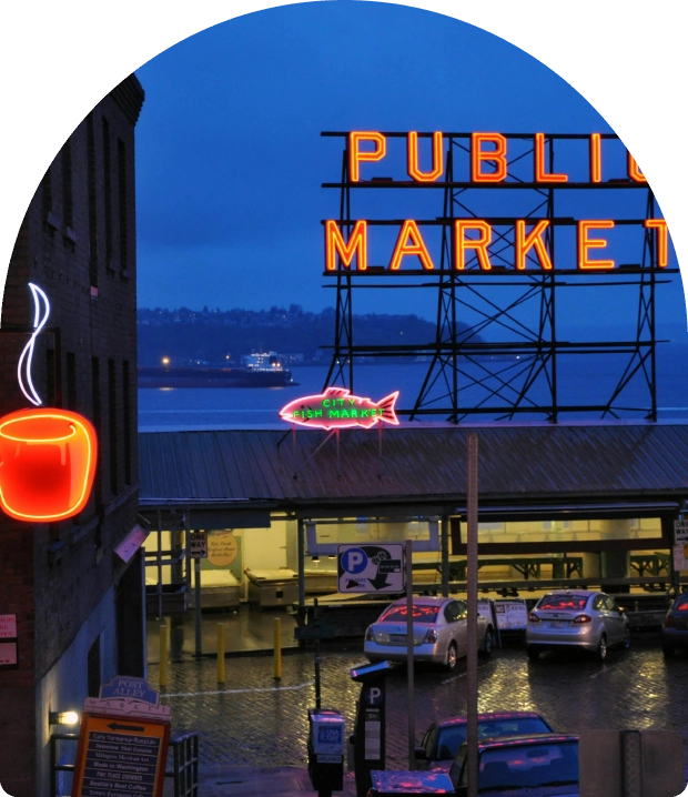 Night view of a public market sign by the waterfront with boats and a steaming coffee cup sign.