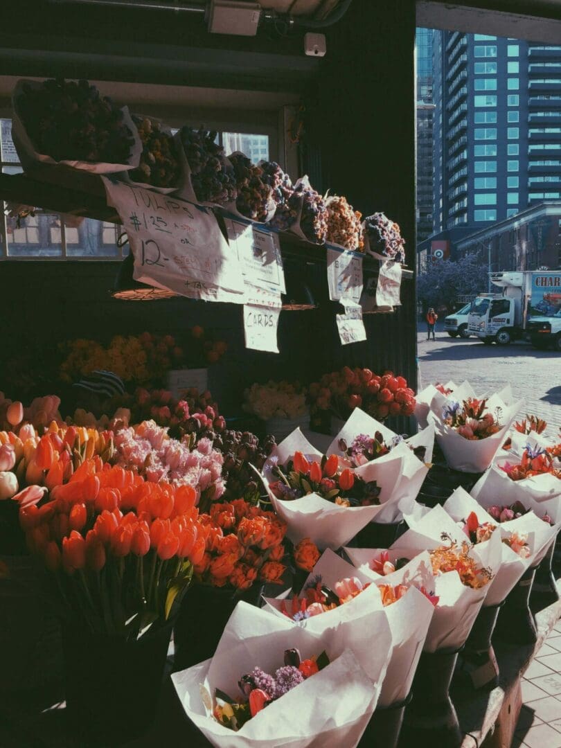 People at a market stall with colorful flower bouquets in an urban setting.