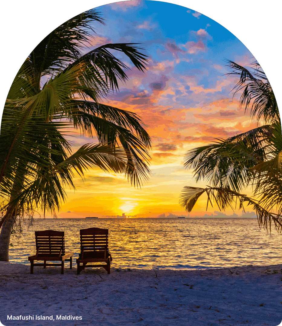 Two lounge chairs on a beach at sunset with palm trees.