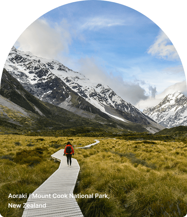 Hiker walking on a boardwalk through a grassy valley in Aoraki Mount Cook National Park.