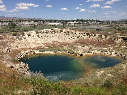 A vibrant blue lake surrounded by a rocky quarry under a partly cloudy sky.