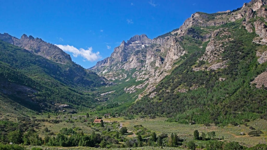 Scenic view of a rocky outcrop overlooking lush green valleys under a cloudy sky.